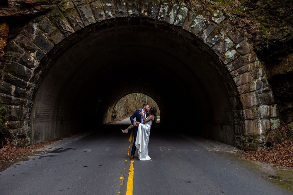 Stone tunnel entrance with yellow dividing line on road and dark interior leading into mountain.