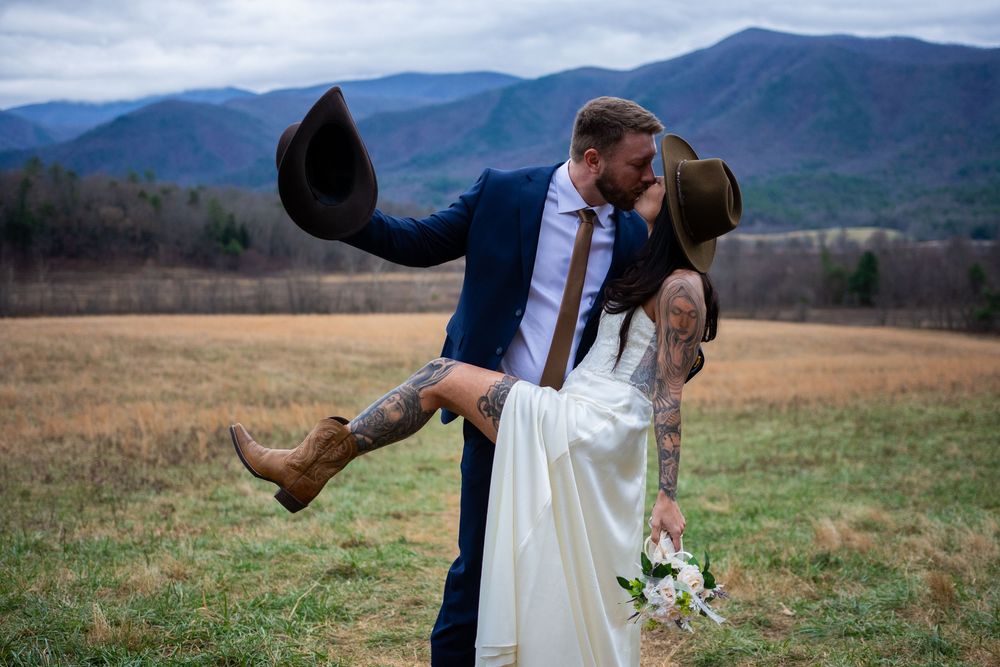 A couple in wedding attire embraces in a scenic mountain field during their outdoor ceremony.