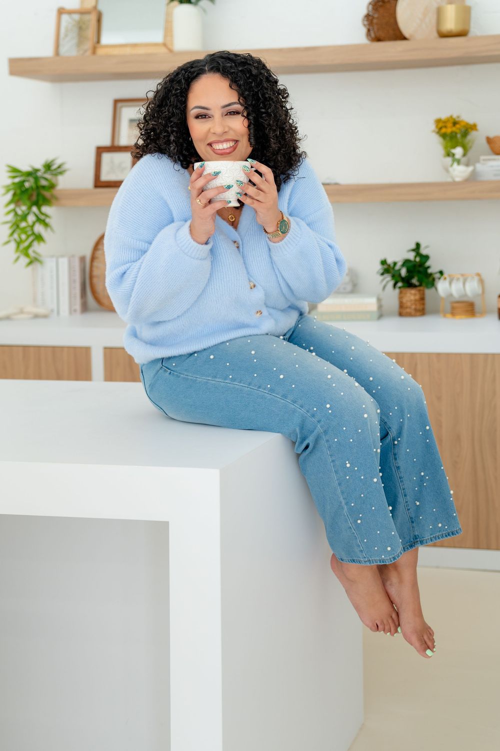 Person lounges on white bench wearing blue cardigan and denim, surrounded by floating wooden shelves.