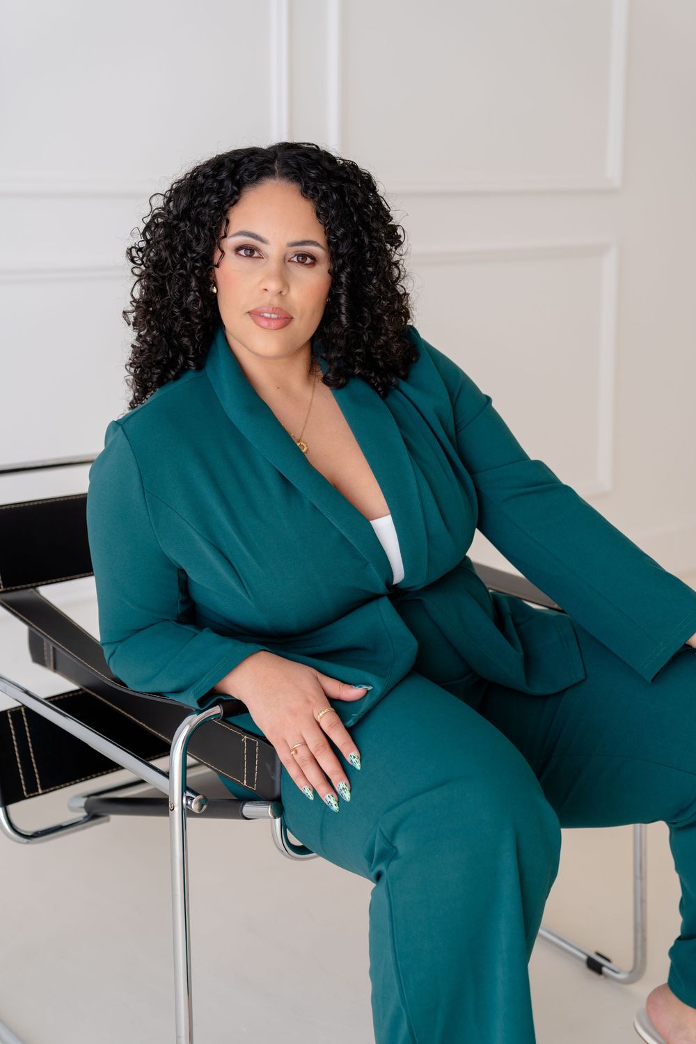 Professional fashion photo series showing model in emerald green blazer posing on modern furniture against white backdrop.