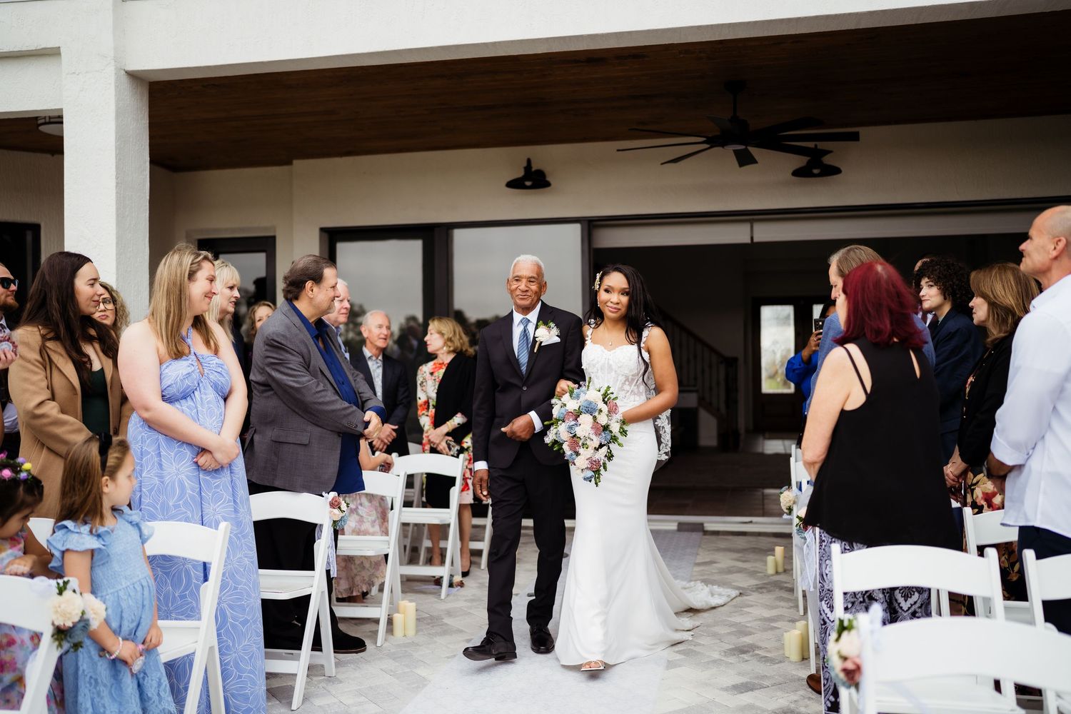 Wedding guests mingle and socialize during an outdoor reception at a covered venue space.