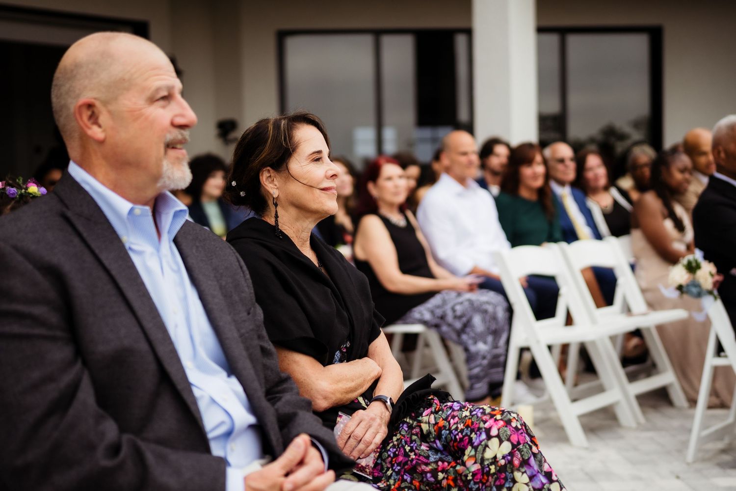 Wedding guests seated in white folding chairs during an outdoor ceremony at dusk.