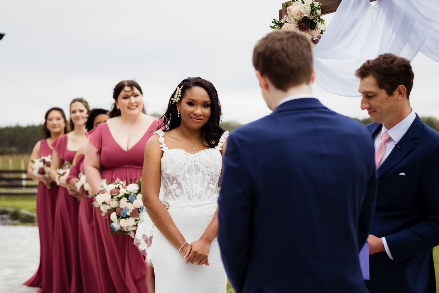 A wedding party stands outdoors in burgundy and navy attire holding bouquets during a formal celebration.