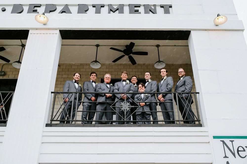 Group of people standing together on a white balcony with railings and a ceiling fan visible above.