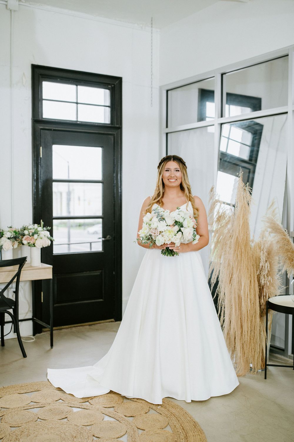 A bride in a classic white wedding gown poses in a bright modern studio space with dried pampas grass decor.