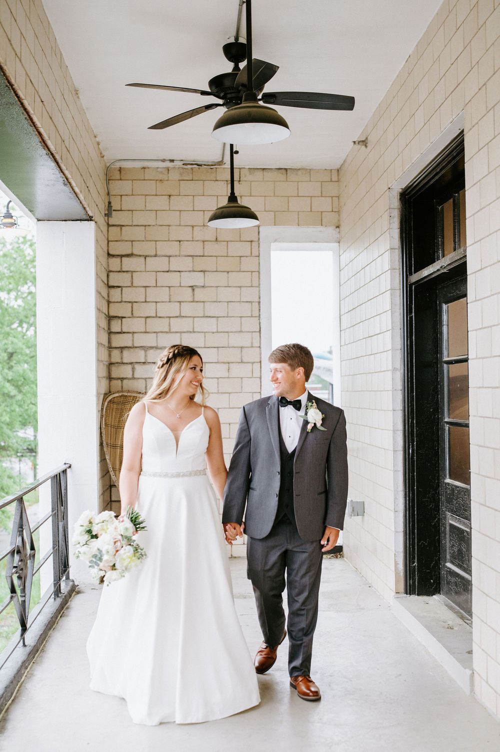 A wedding couple walking together on a white porch with brick walls and black trim in a series of progressive shots.