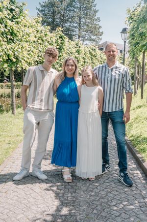 Family of four posing outdoors on a sunny day, dressed in elegant attire on a tree-lined cobblestone path.