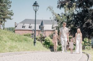 Family of four walking on cobblestone path past brick building and lamp post on sunny day.