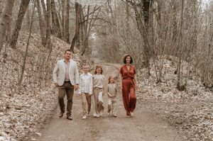 Family of five walking on a wooded trail in autumn, dressed in elegant earth tones for a portrait.