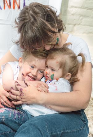 A mother hugging two young paint-covered children, sharing a joyful and loving moment together.