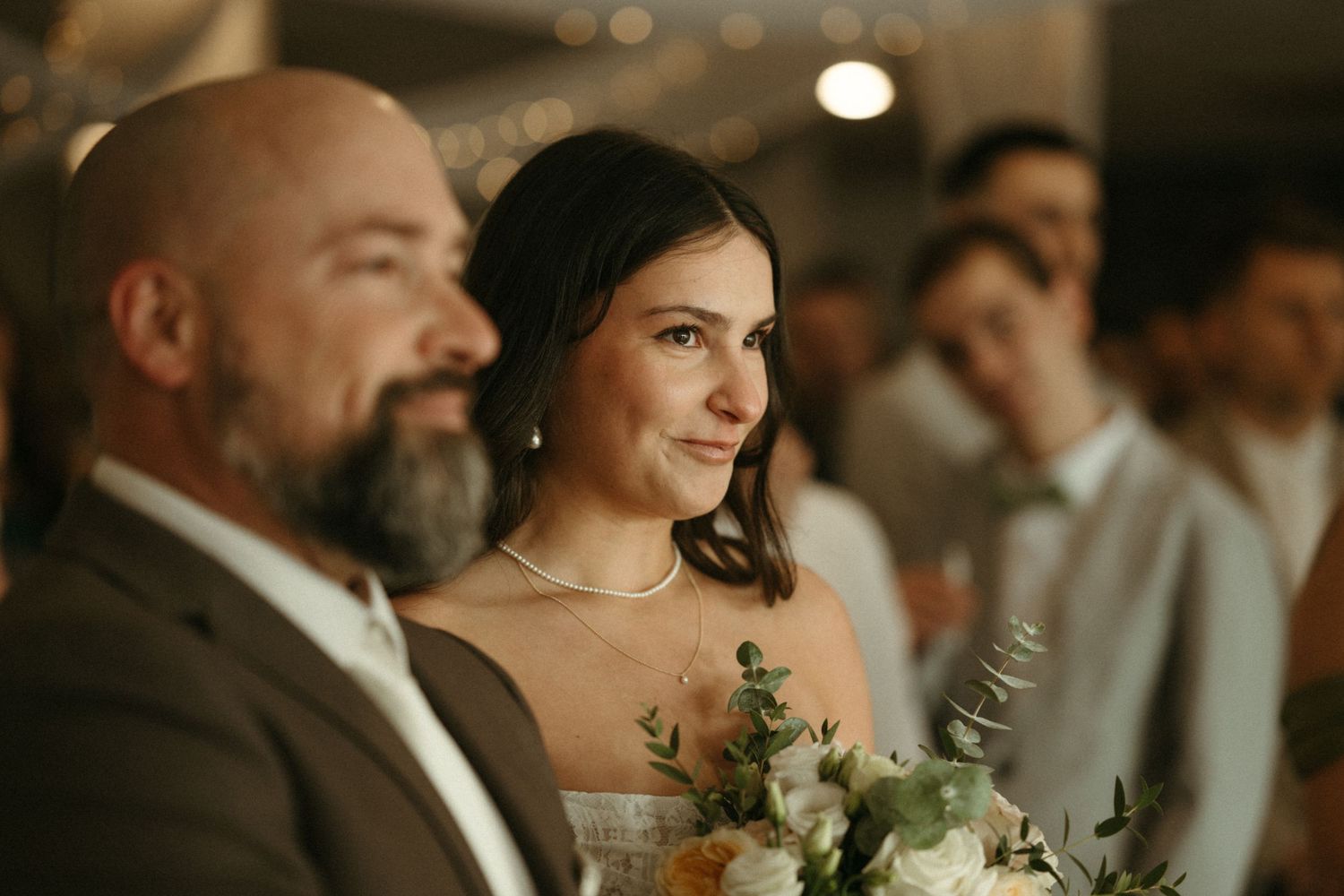 Wedding guests seated at a reception watch intently with joyful expressions during an emotional moment.