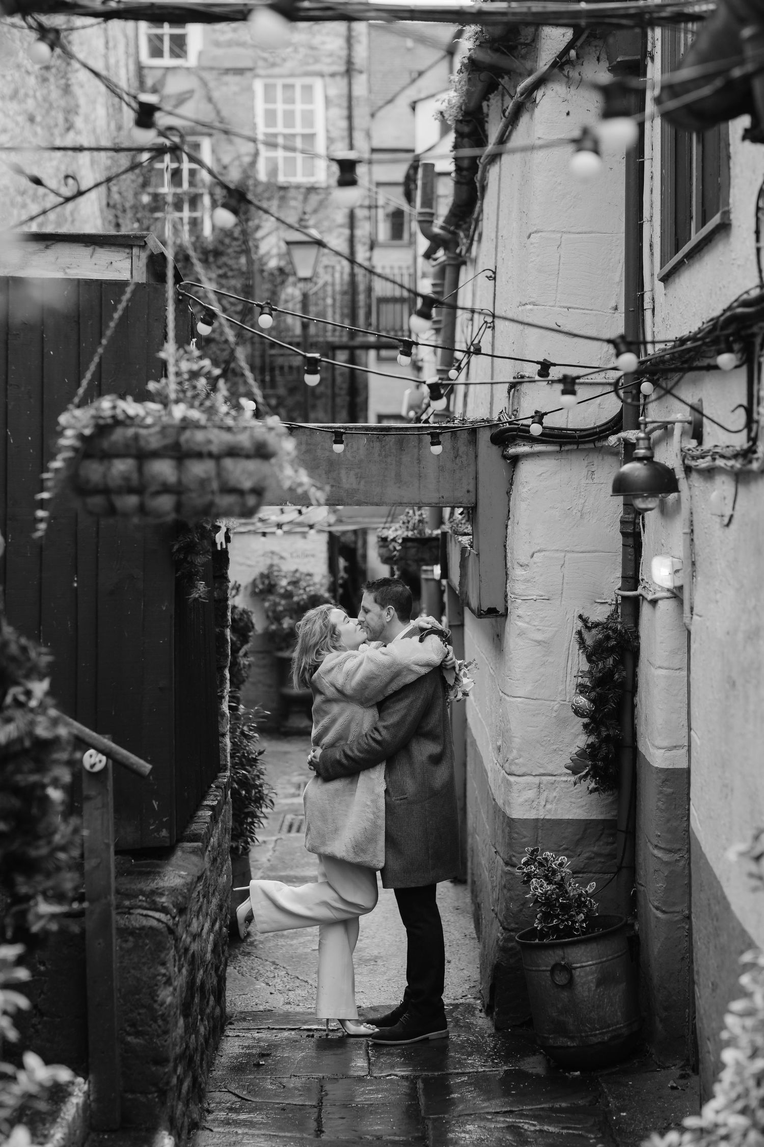A black and white series of intimate moments captured in an alleyway with string lights.