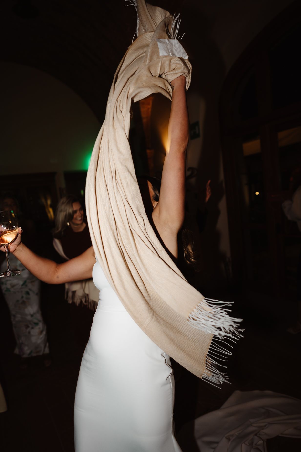 A person in a white wedding dress dances with a flowing shawl in dim lighting.