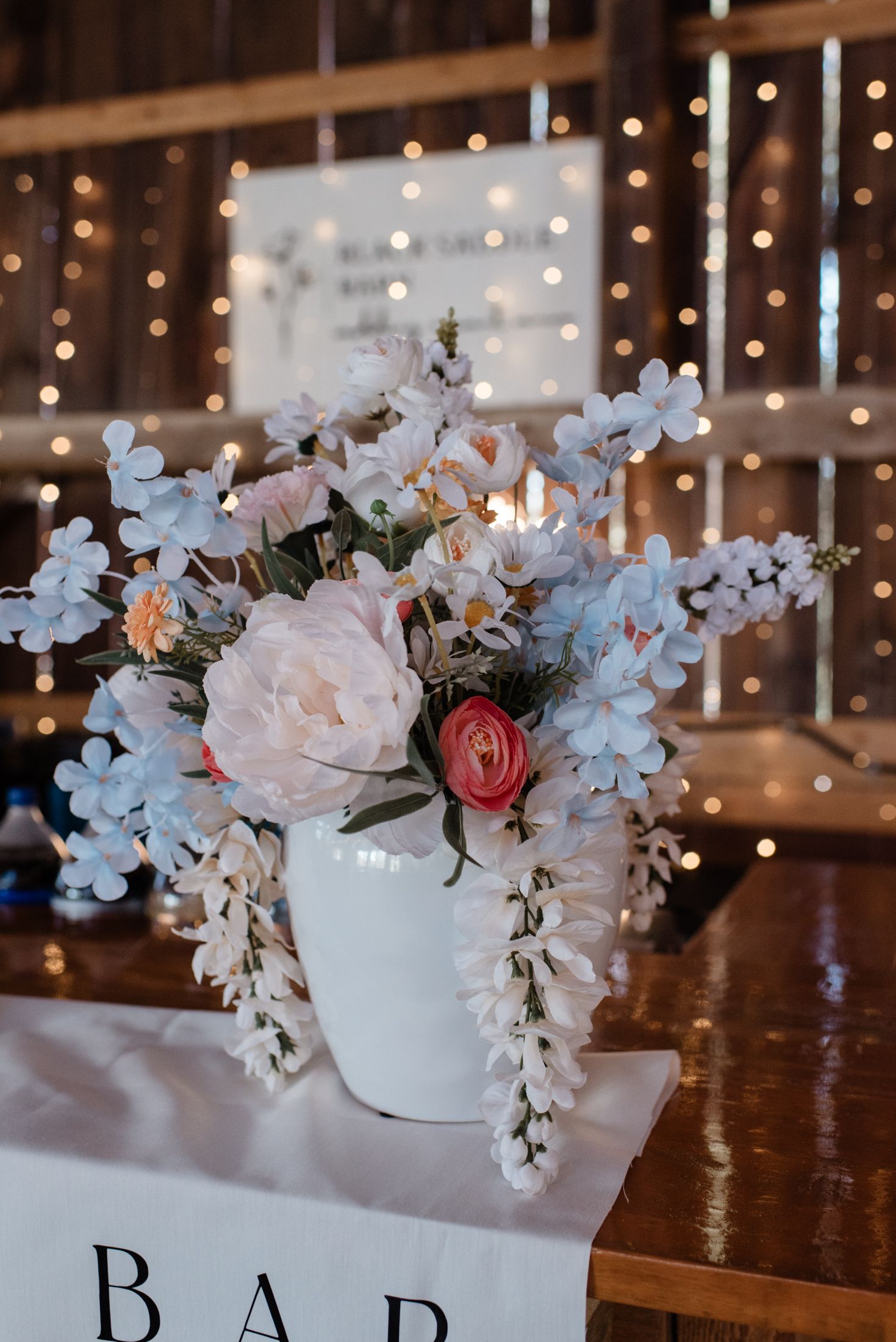 Wedding reception decor with white floral centerpieces and string lights creating a romantic ambiance at a bar area.