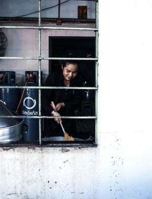 Smiling woman in black cooking stir fry in a small kitchen window.