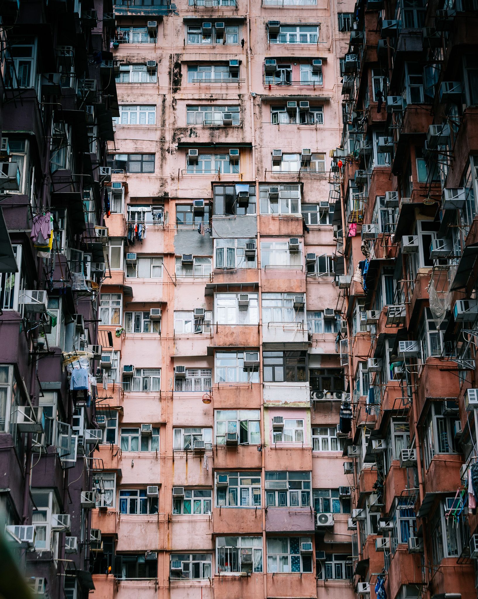 Dense facade of a towering pink residential apartment building with air conditioners in Hong Kong.