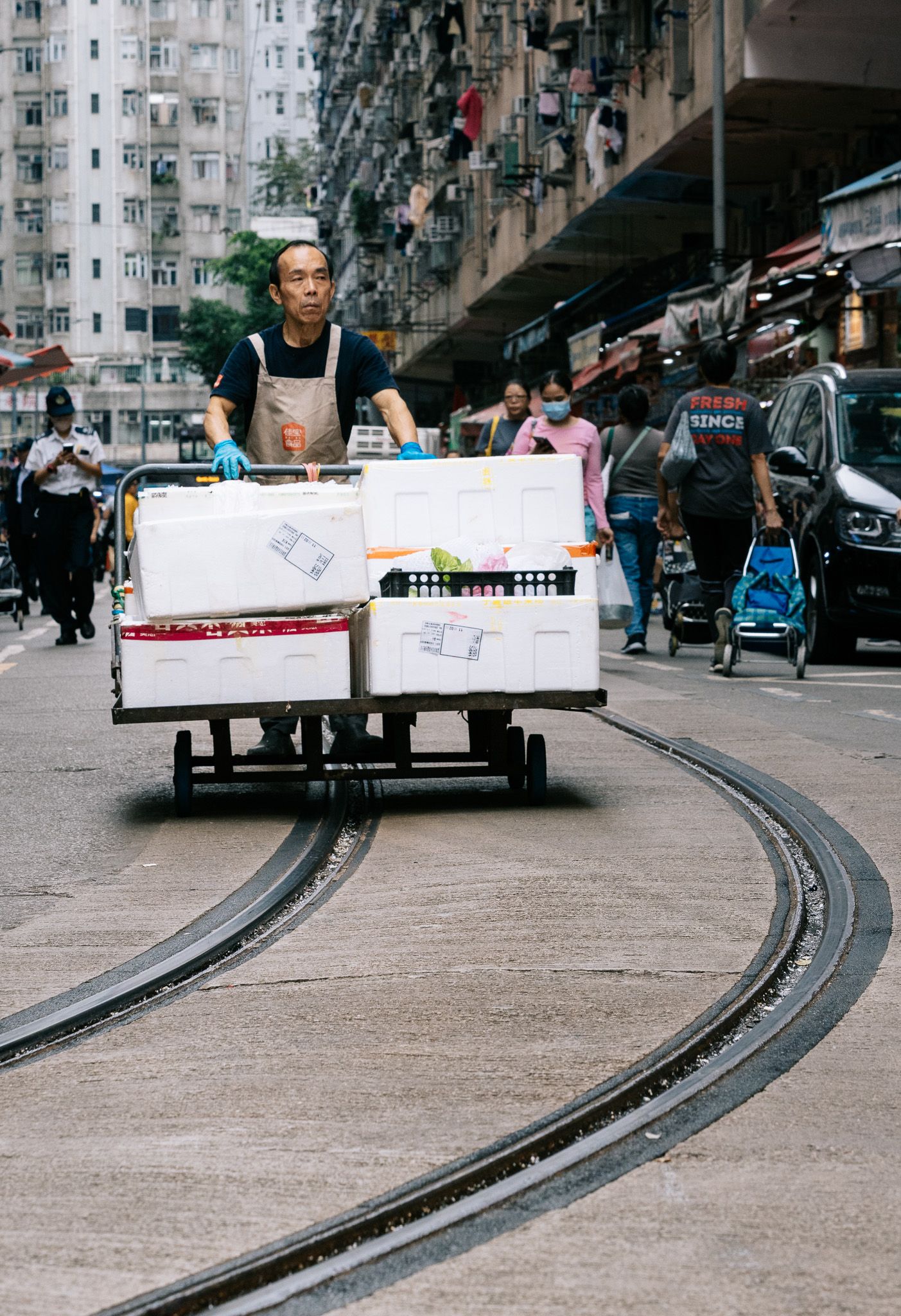 A worker pushes a heavy cart loaded with boxes along tram tracks on a busy Hong Kong street.
