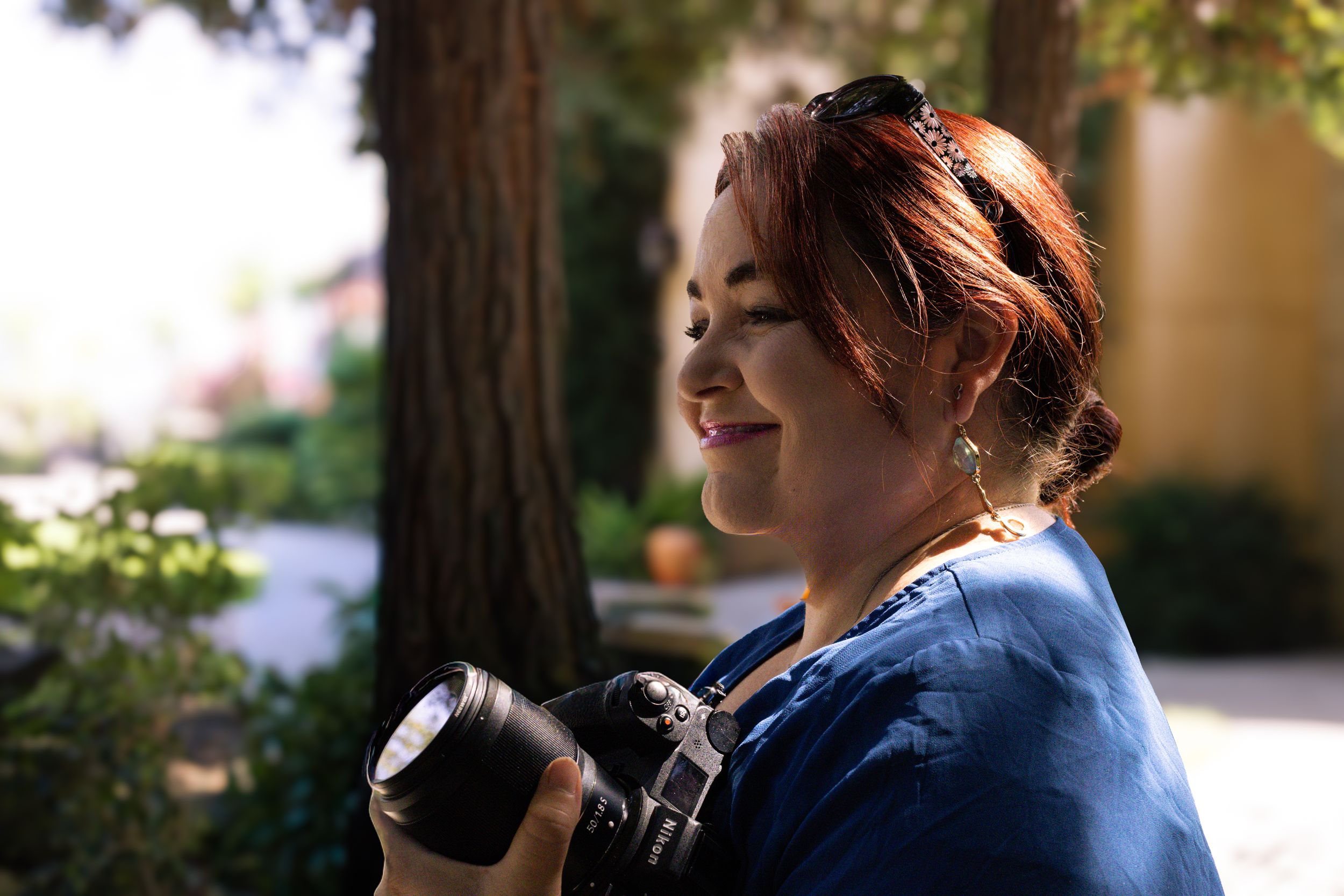 Photographer in blue shirt smiles while reviewing photos on digital camera outdoors.