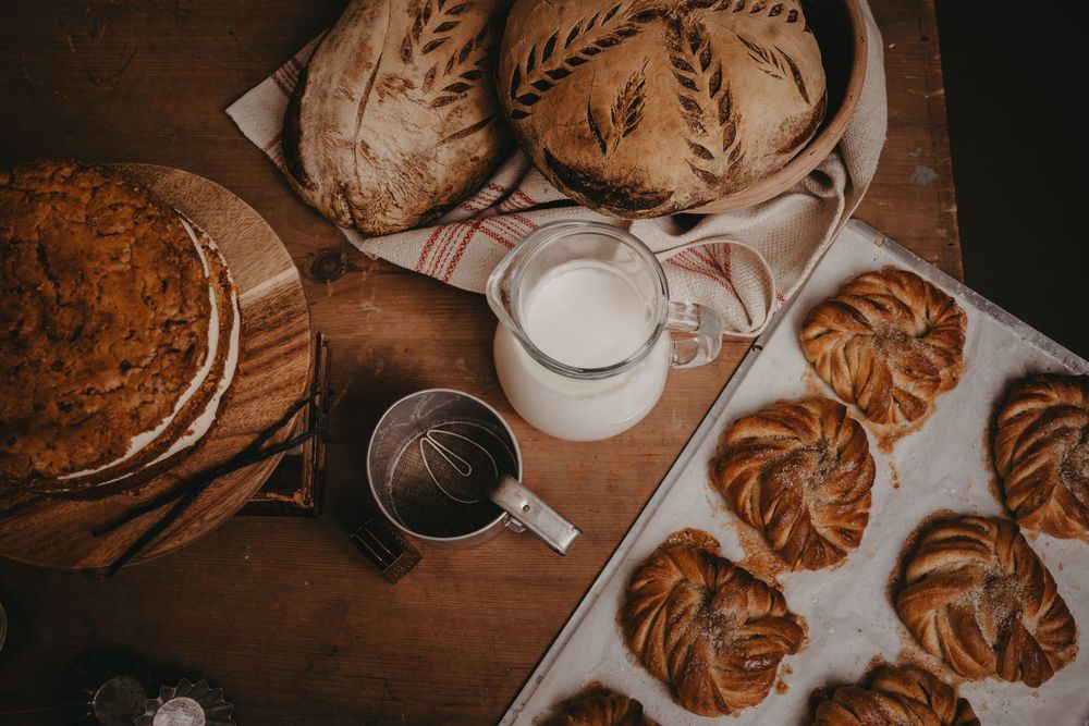 Freshly baked cinnamon buns and glasses of milk arranged on a rustic wooden table in warm lighting.