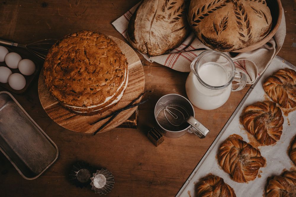 Overhead view of freshly baked pastries, croissants, and bread with a glass of milk on rustic wooden table.