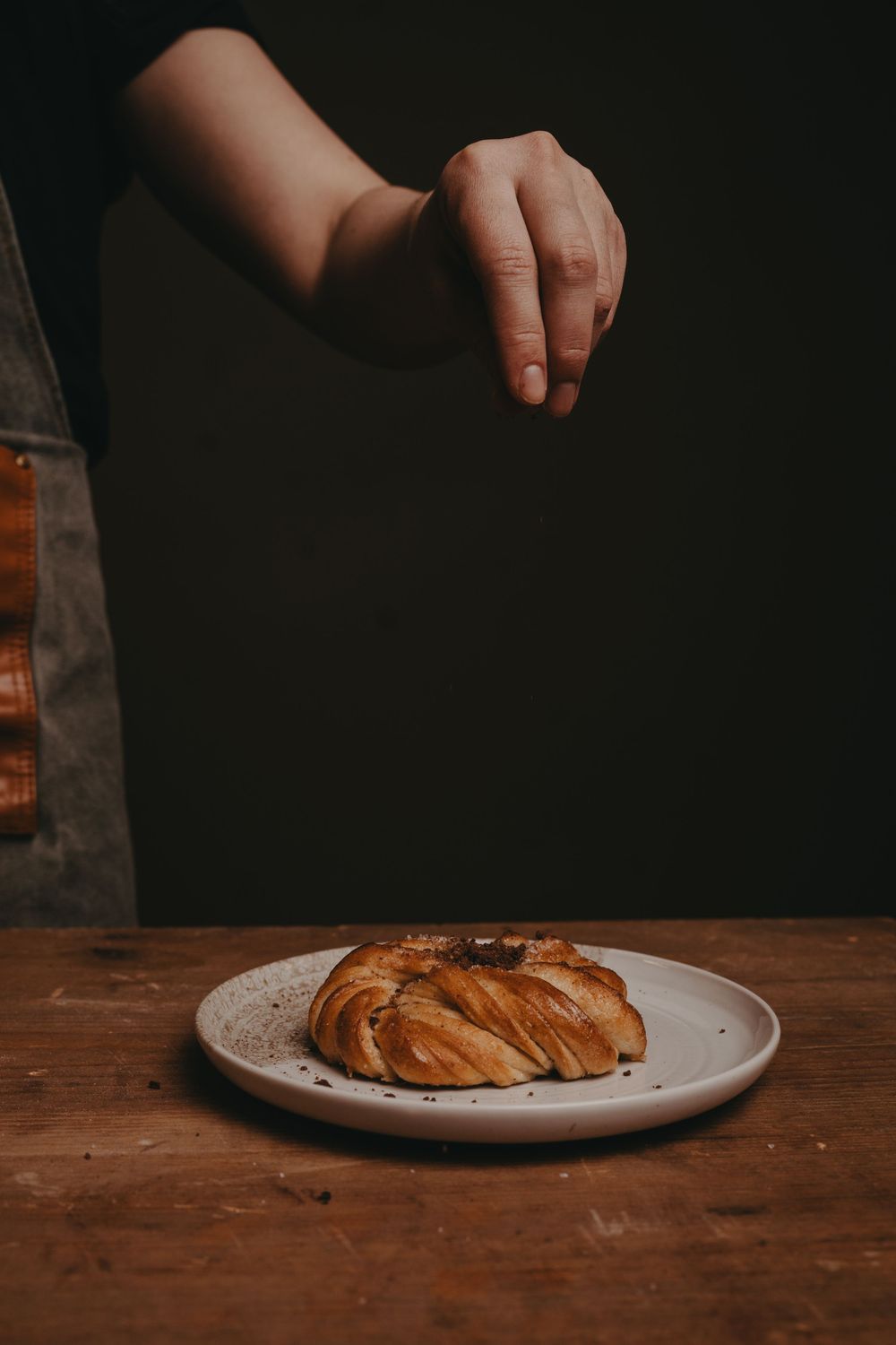 Hand reaching for a freshly baked croissant on a white plate against a dark wooden table surface.