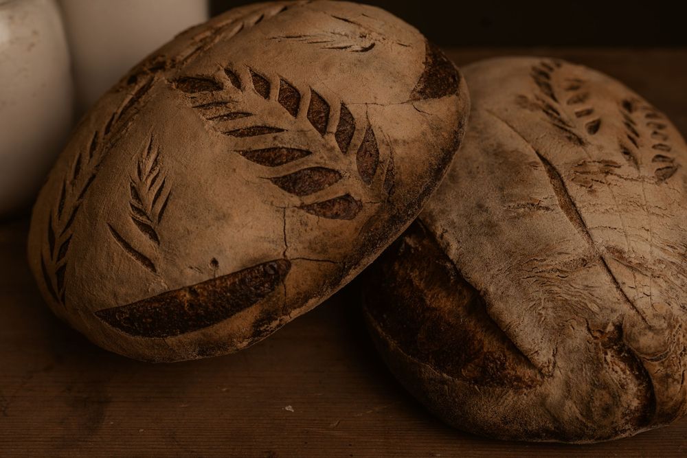 Two rustic artisan bread loaves with leaf pattern designs scored into their brown crusts shown in sepia tones.