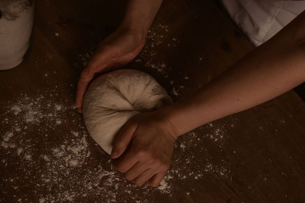 Hands kneading fresh dough on a floured dark surface in moody lighting.