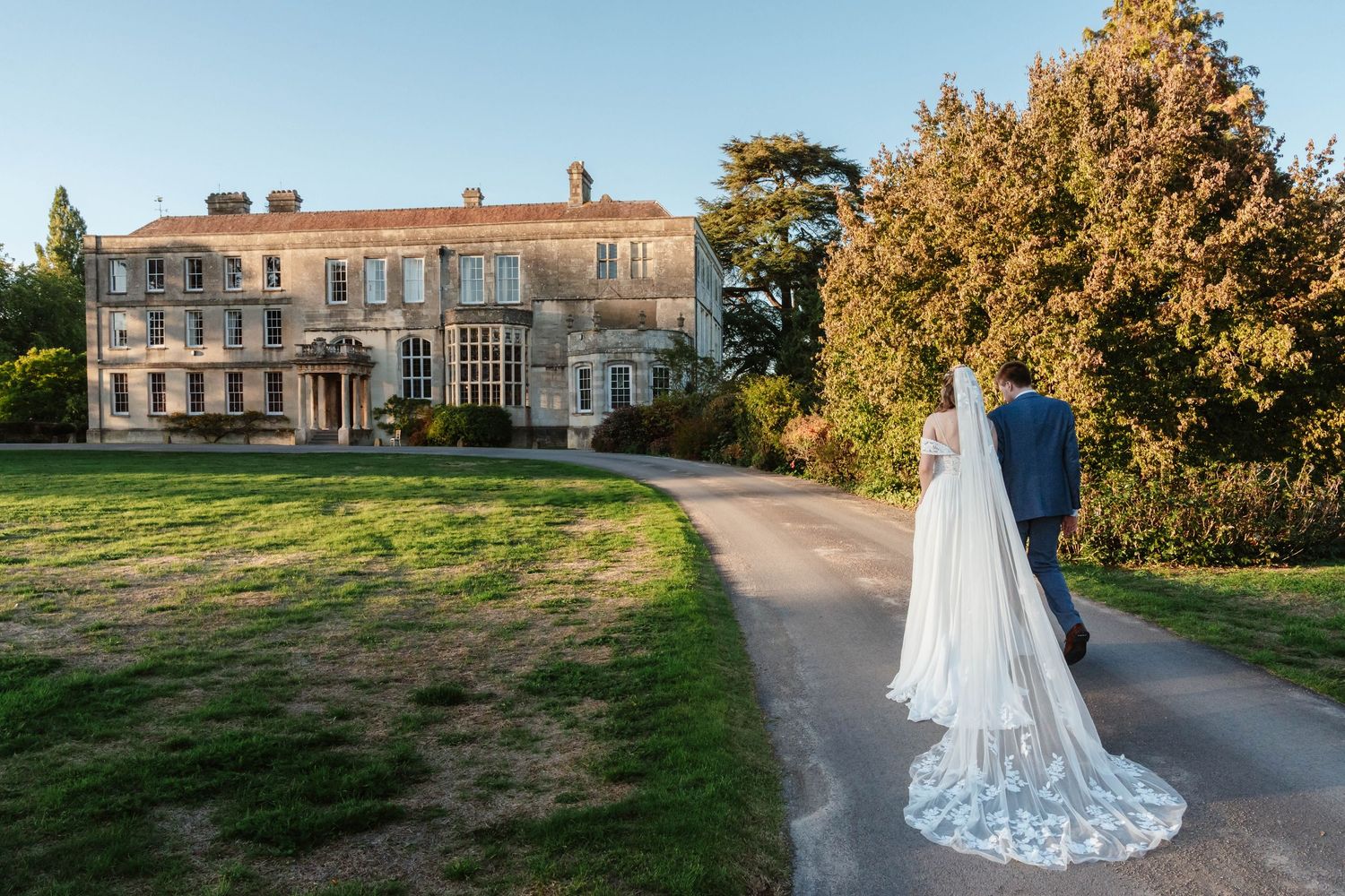 Exterior of Elmore Court manor house wedding venue Gloucestershire with bride and groom walking towards manor house