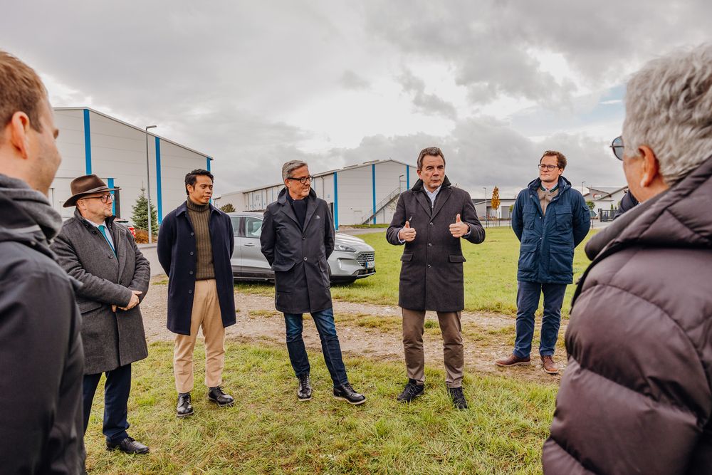 A group of people having a discussion while standing in a circle on grass with cloudy skies overhead.