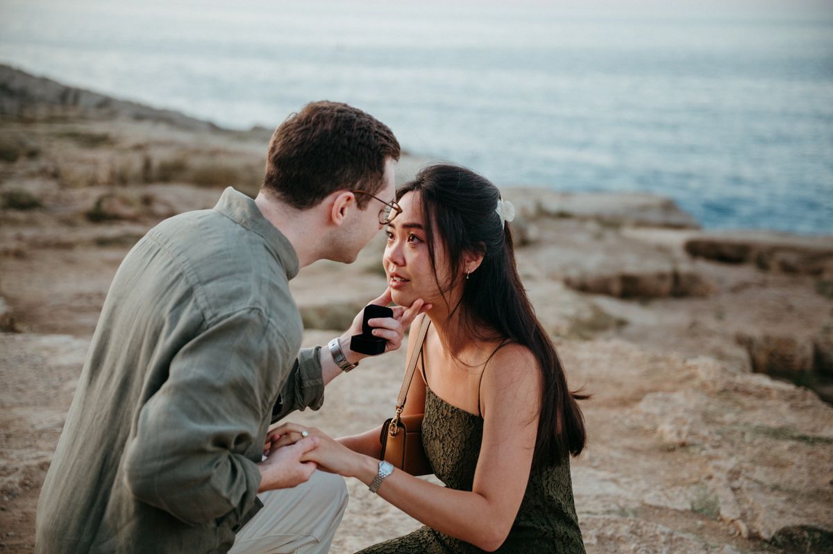 Couple shares tender moments together on rocky coastal beach during sunset photoshoot.