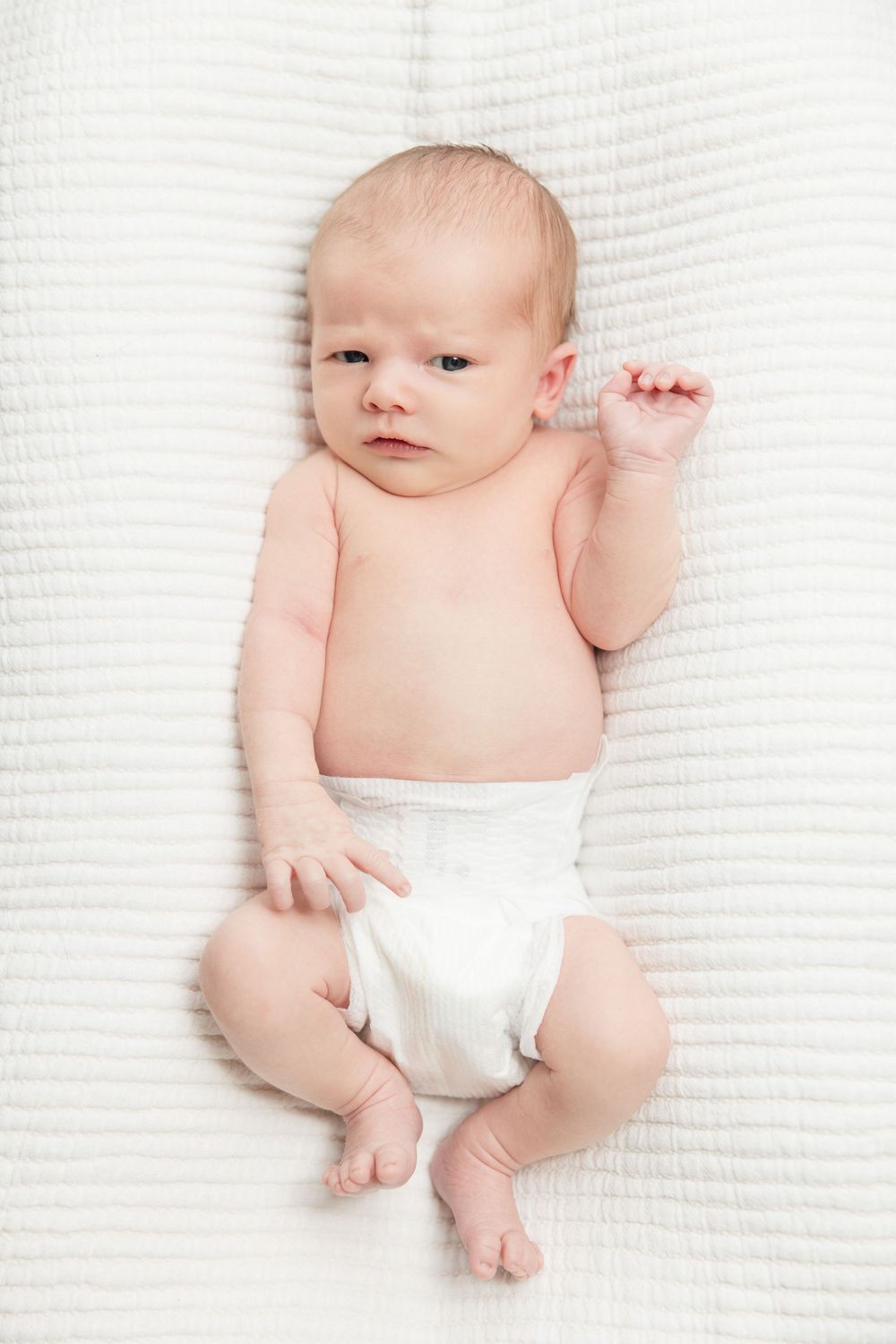 Newborn baby wearing white diaper lying on textured white blanket in four different poses.