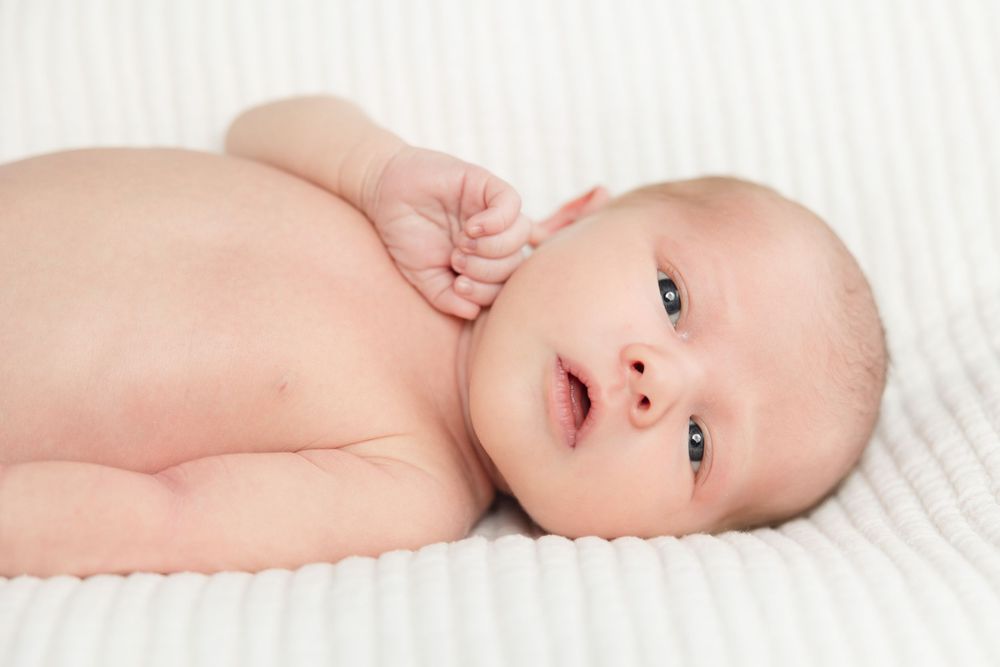 Sweet newborn baby lying on white blanket in different poses during professional photo session.