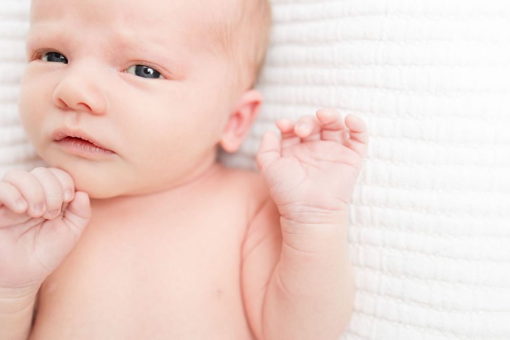 A newborn baby lies peacefully on white fabric while wrapped in soft pink swaddling material.