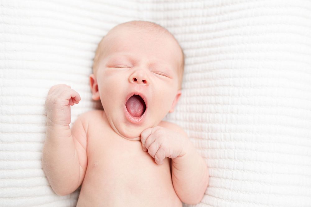 Adorable baby laughing while lying on soft white blanket with arms raised in joyful expression.