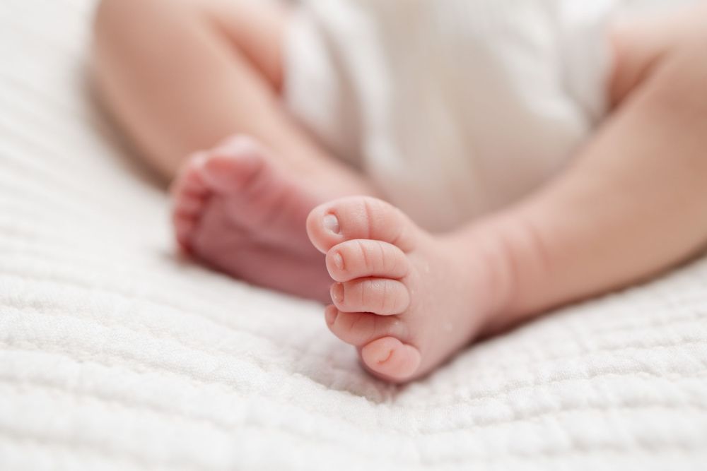 Close-up of tiny newborn baby feet and toes resting on soft white blanket.