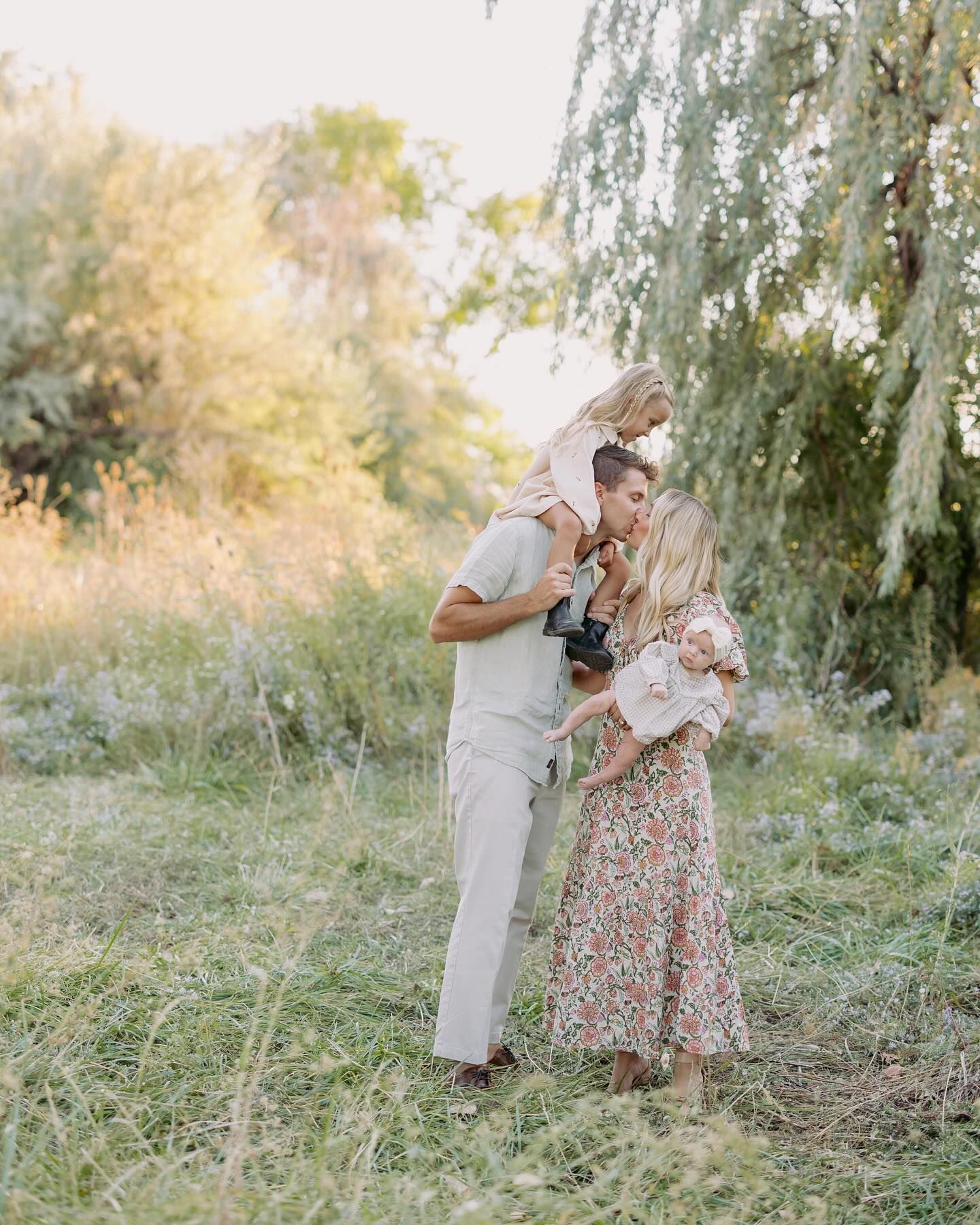 A couple shares a romantic moment under a willow tree in a dreamy outdoor setting during golden hour.
