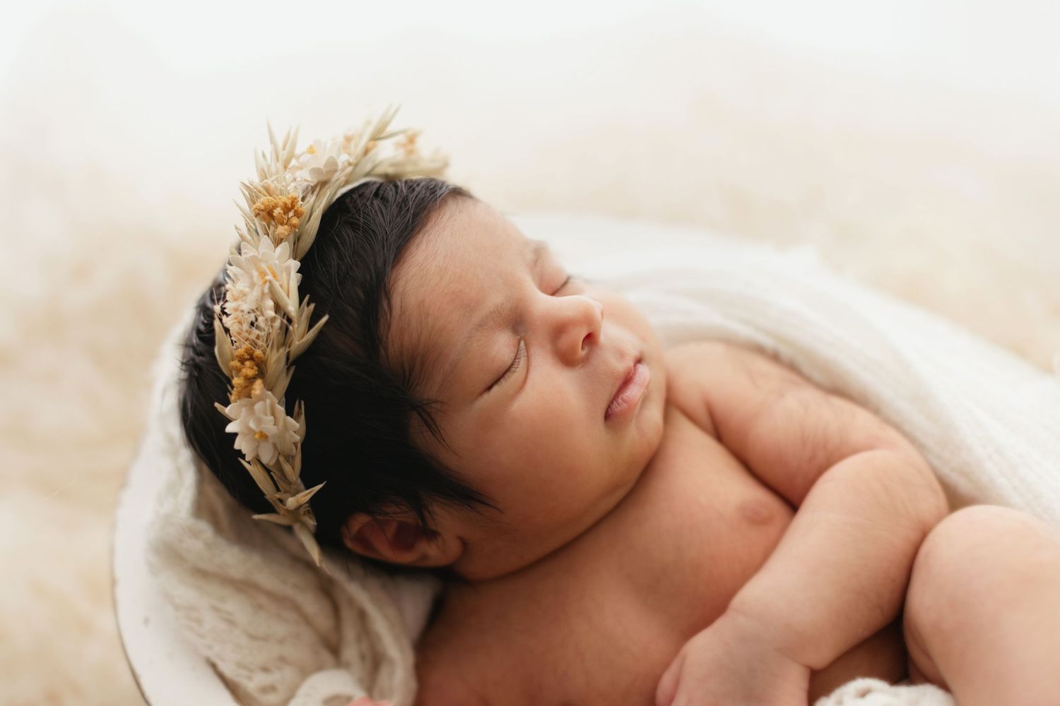 Peaceful sleeping newborn wearing a delicate gold crown nestled in soft beige blankets during professional photo session. Elizabeth Lang Pho