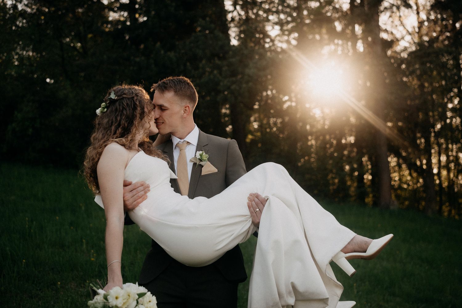 A couple shares an intimate moment in a wooded area during golden hour sunset.