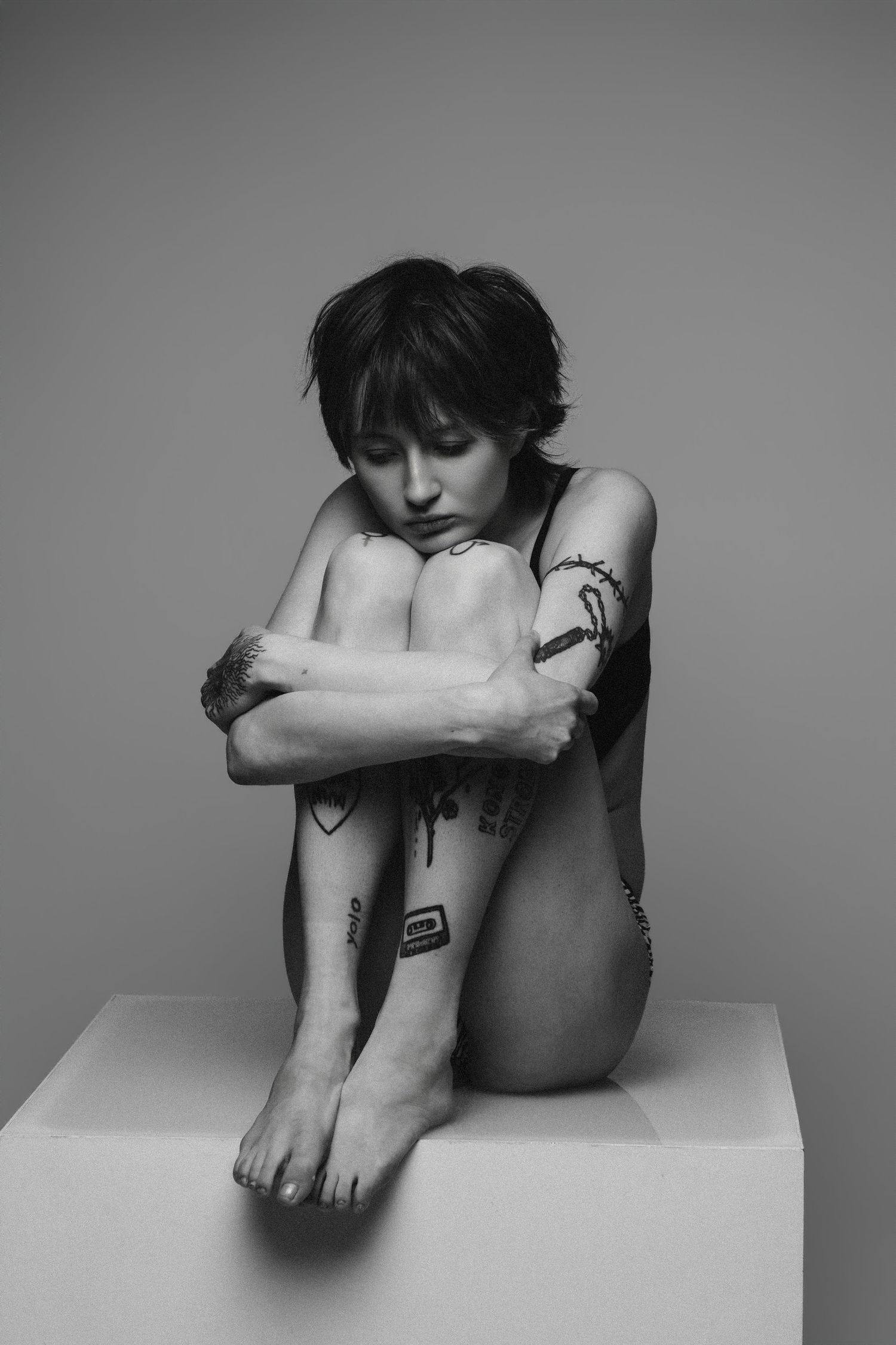 Black and white artistic photo series showing someone in fetal position on white surface expressing vulnerability and solitude.