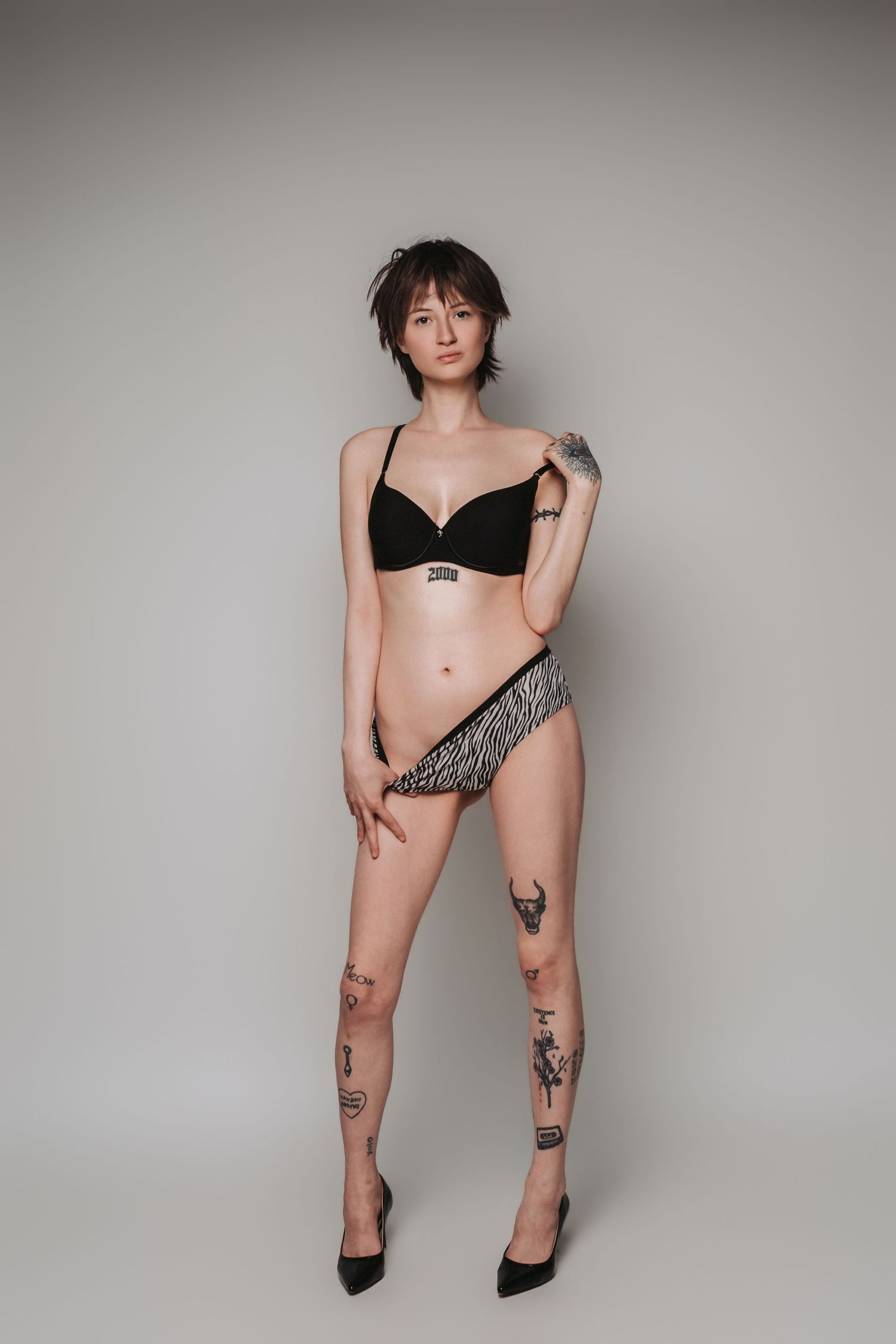 A person in black lingerie and zebra print underwear poses against a light gray studio backdrop.
