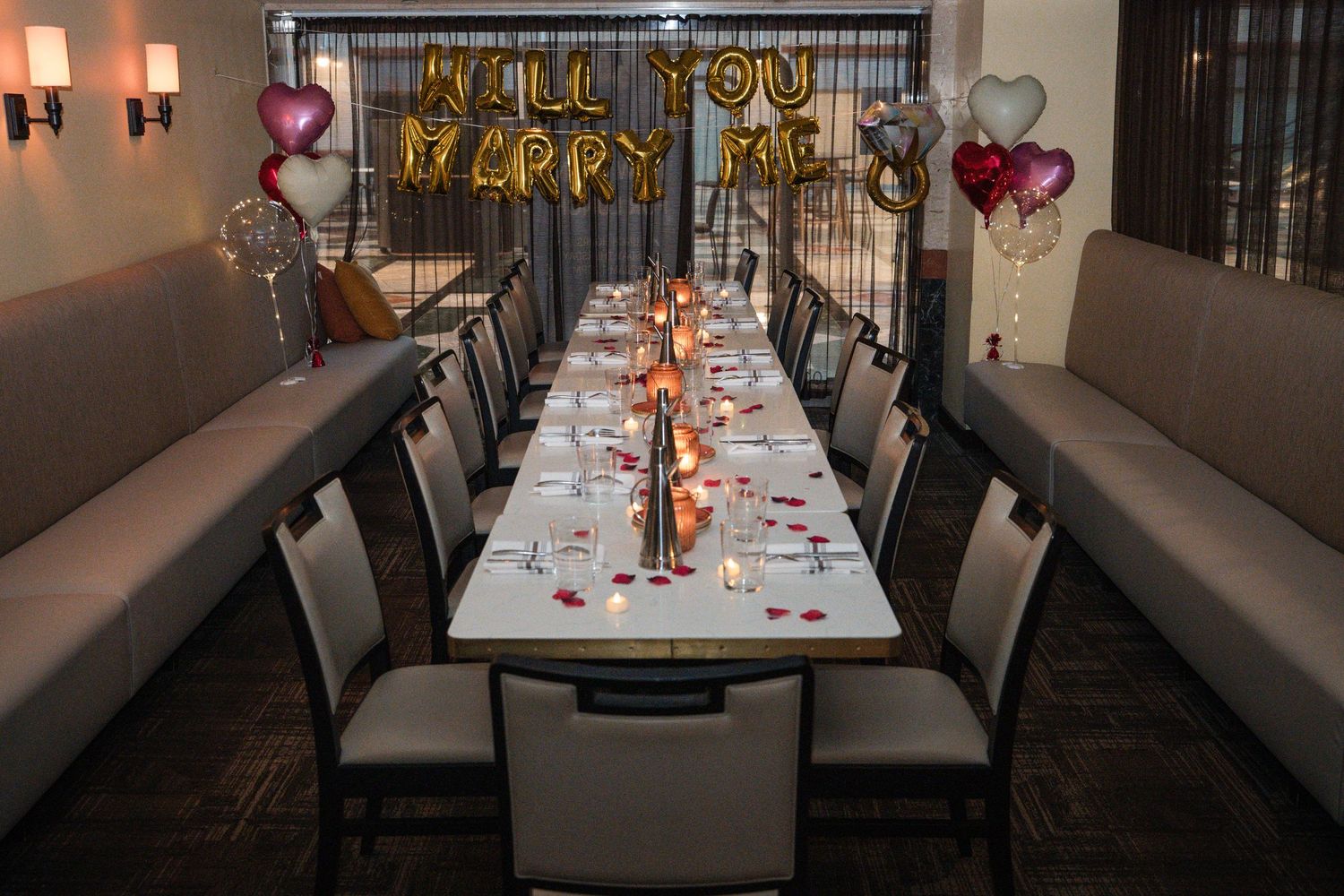 Elegant restaurant table setup with pink and gold decor, balloons, and romantic lighting for a special occasion.