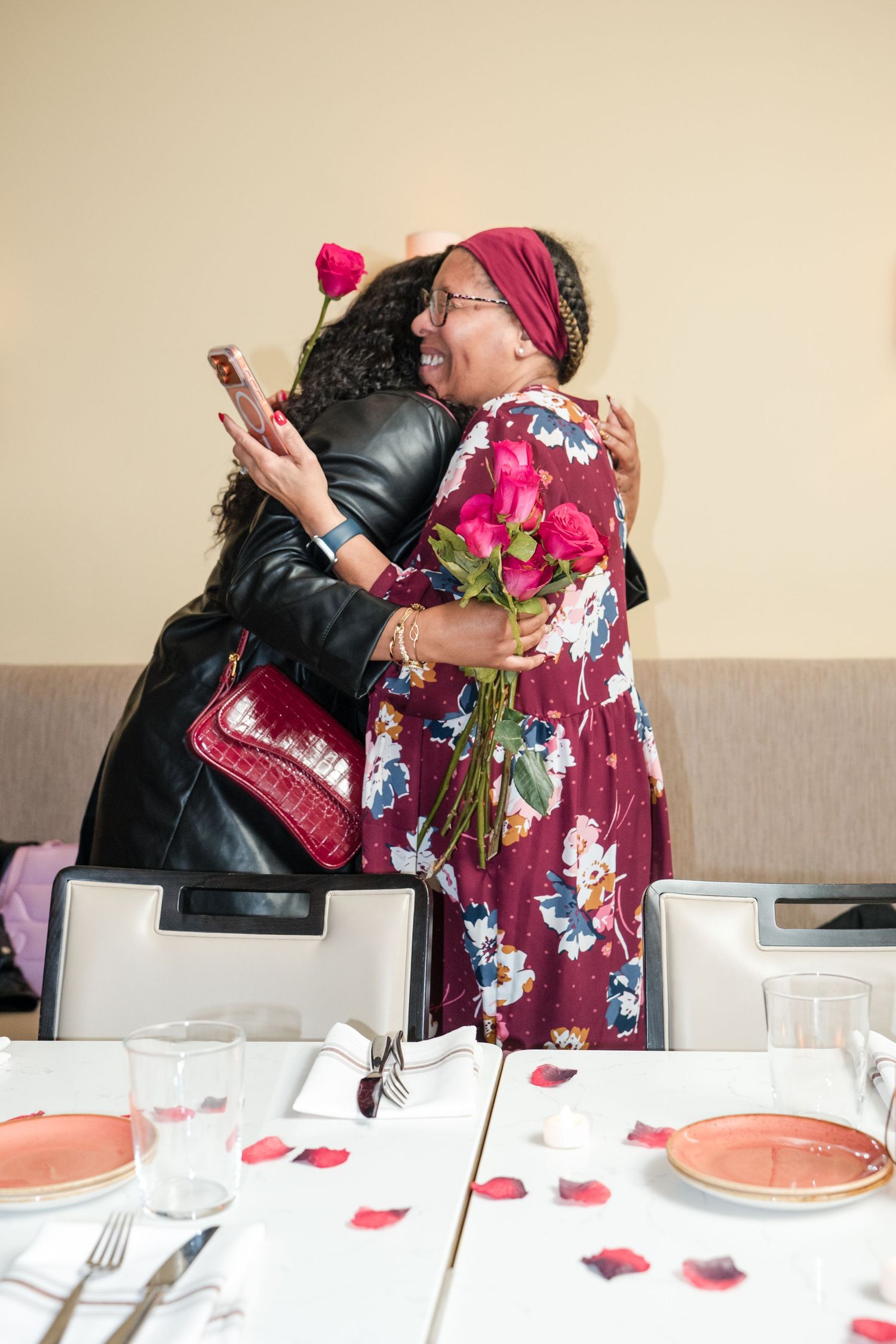 Two people embrace and share a romantic moment at a table decorated with rose petals and candlelight.