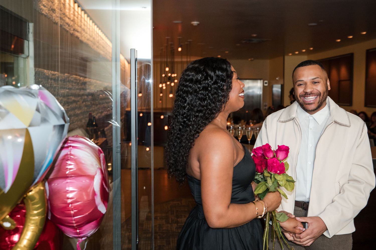 Wedding reception guests mingle and celebrate in an elegantly lit indoor venue with glass walls.
