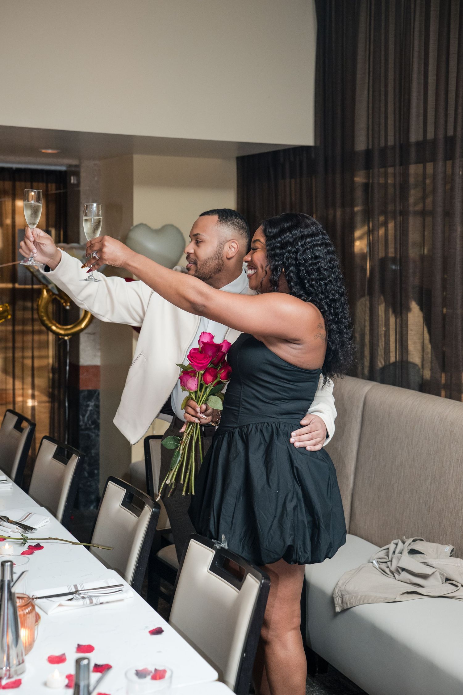 People celebrating with drinks and flowers in an elegant dining room with gray seating.