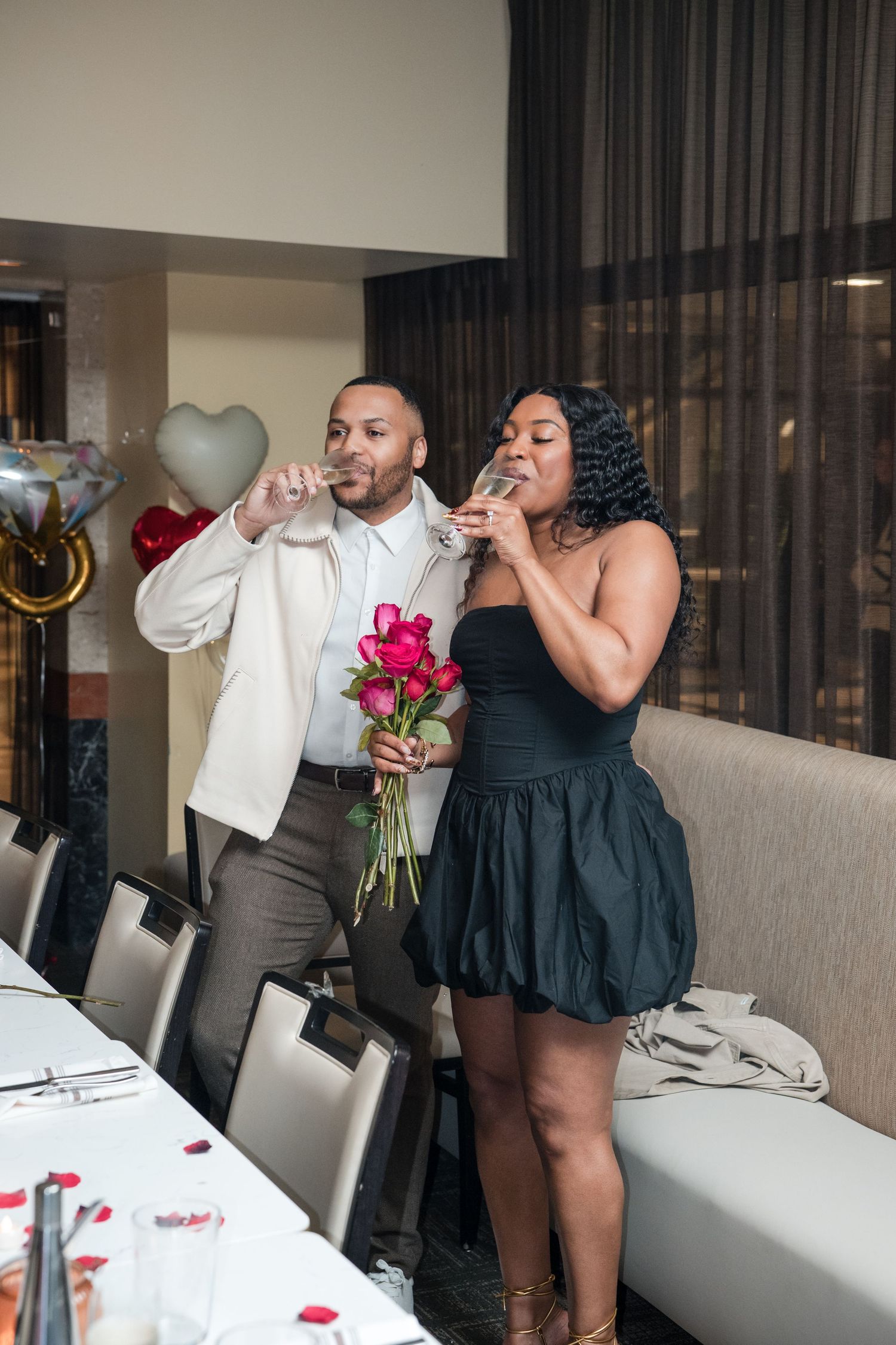 Couple enjoying drinks and roses during a romantic dinner celebration at an upscale venue.