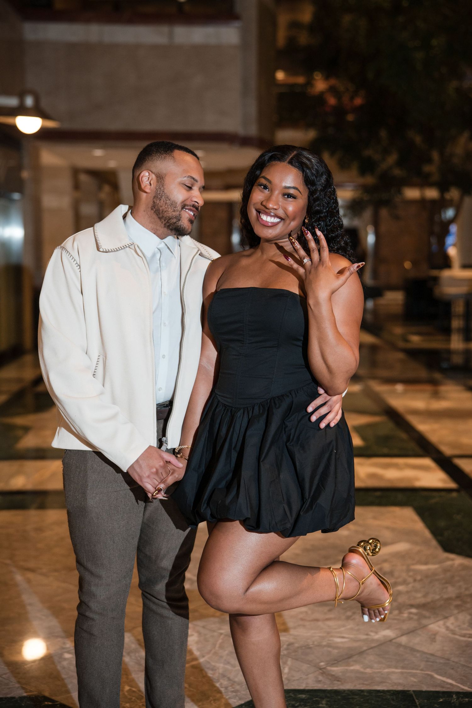 Playful engagement photo session with couple posing against urban architectural backdrop.
