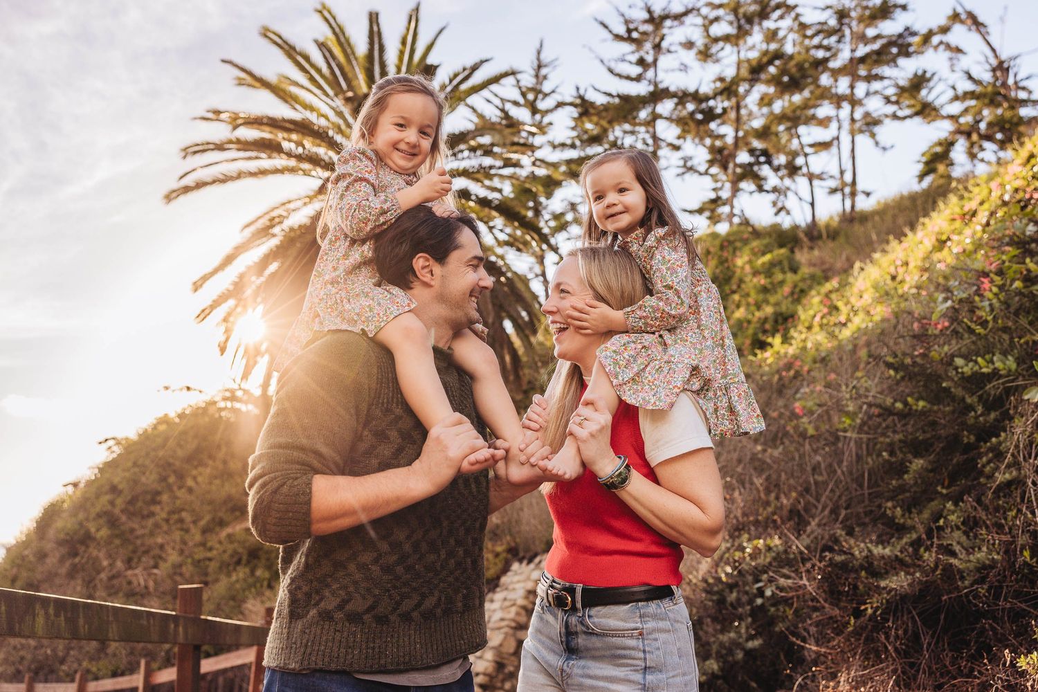 A family enjoys a playful moment together outdoors at sunset with a palm tree silhouetted in the background.