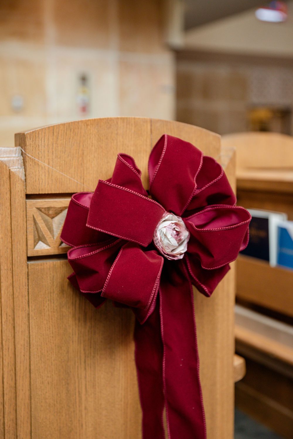 A burgundy velvet ribbon bow decorates the side of a wooden church pew in a row of similar decorations.