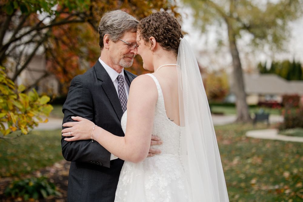 A couple shares an intimate moment outdoors during their autumn wedding ceremony among golden leaves.