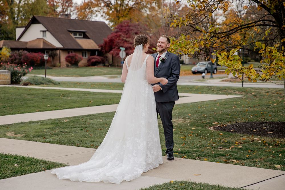 A couple shares a joyful moment on their wedding day against an autumn backdrop with fall foliage.